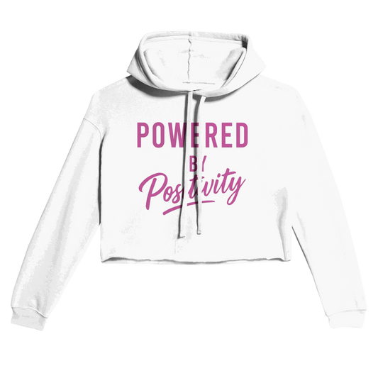 White motivational women's cropped hoodie with "Powered by Positivity" text in pink, featuring raw hem and drawstrings