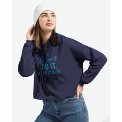 Woman wearing navy blue cropped hoodie with "Dream It. DO IT. ACHIEVE IT." motivational text and raw hem, paired with jeans and white beanie