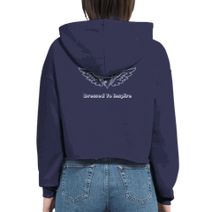 Woman wearing navy cropped hoodie with "Dressed To Inspire" and wing logo on back, paired with blue jeans, motivational fashion sweatshirt Dream It. DO IT.