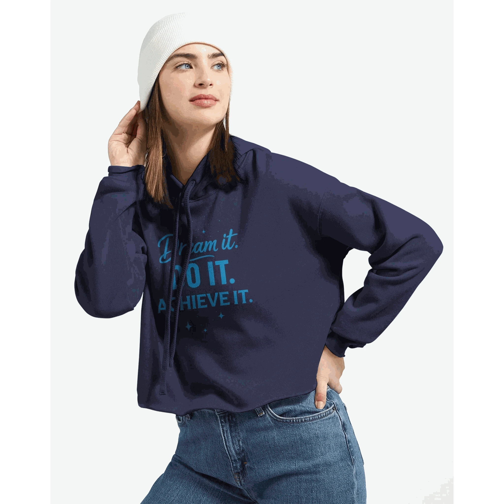Woman wearing navy blue cropped hoodie with "Dream It. DO IT. ACHIEVE IT." motivational text and raw hem, paired with jeans and white beanie