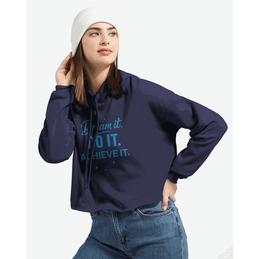Woman wearing navy blue cropped hoodie with "Dream It. DO IT. ACHIEVE IT." motivational text and raw hem, paired with jeans and white beanie