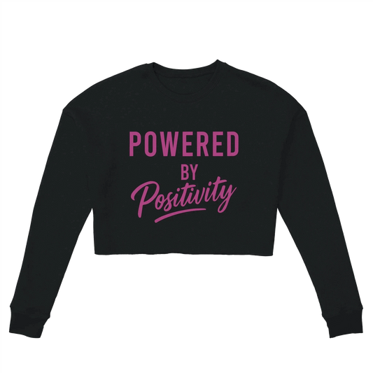 Black women's cropped sweatshirt with "Powered by Positivity" text in pink, motivational crop top with relaxed fit and dropped shoulders