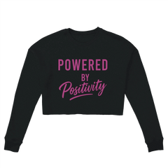 Black women's cropped sweatshirt with "Powered by Positivity" text in pink, motivational crop top with relaxed fit and dropped shoulders